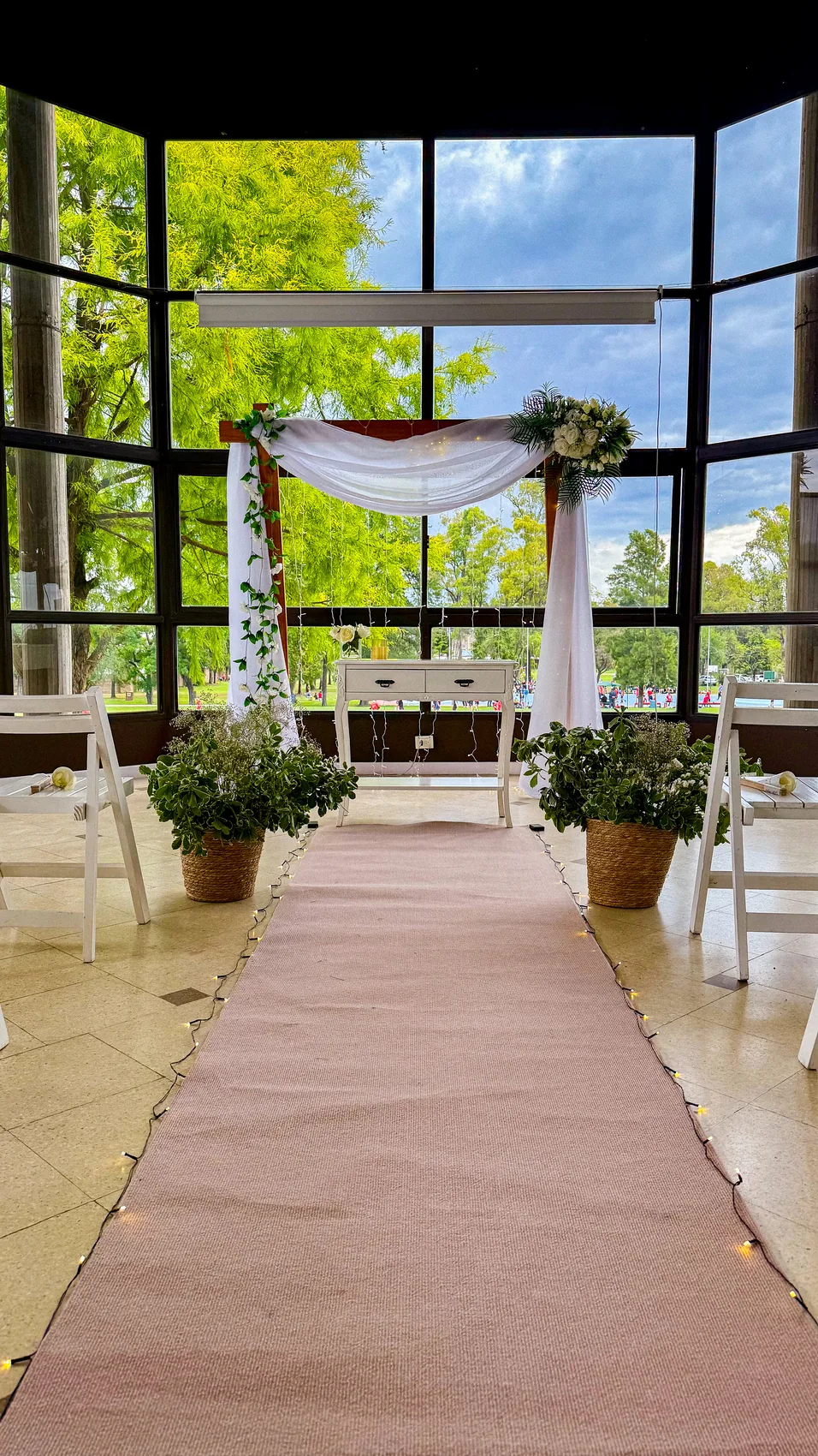Ceremonia de boda con arco de madera, cortinas de gasa, guirnaldas de flores y alfombra de camino