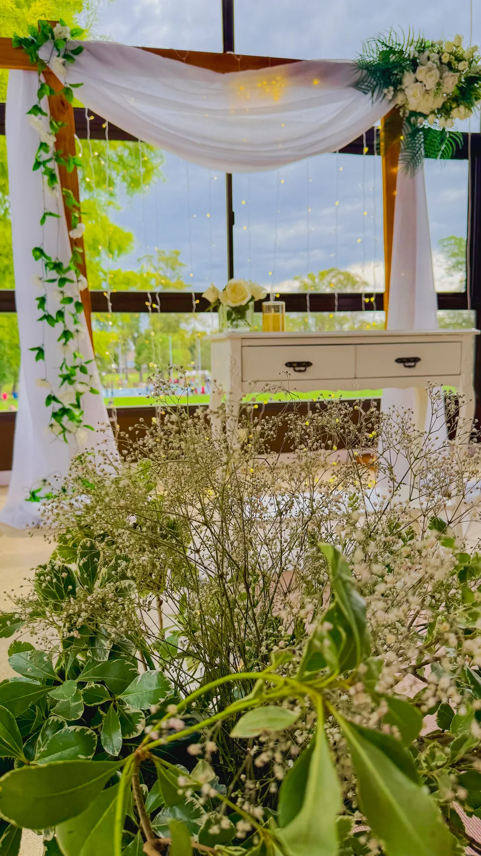 Ceremonia interior con paniculata en primer plano, mueble blanco y cortinas de luces