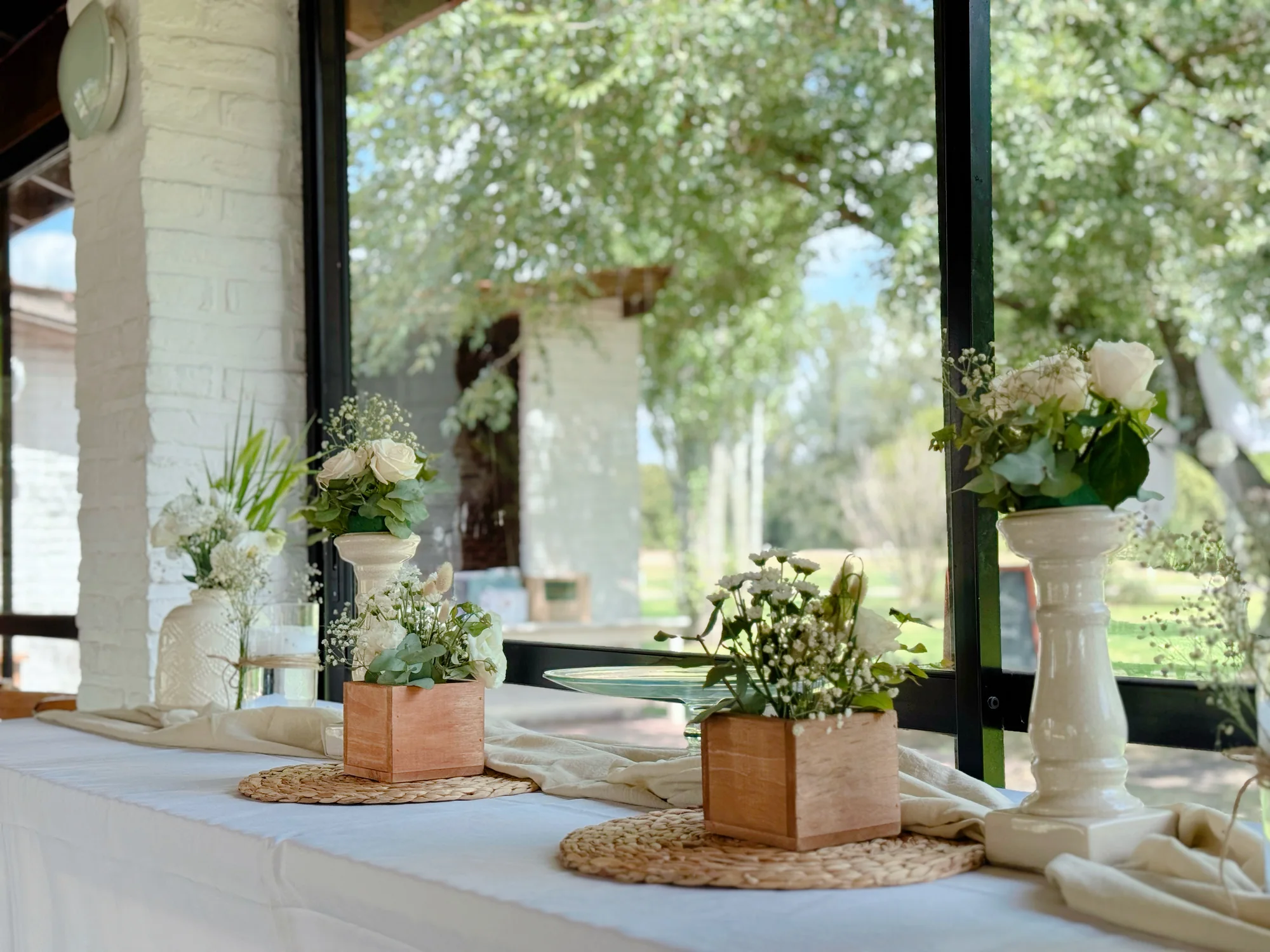 Mesa de recepción con centros en cajas de madera, rosas blancas, paniculata y candelabros de cerámica